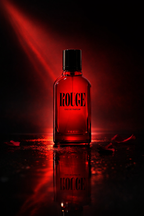 Rouge Eau de Parfum red bottle with black cap lit by red light on a dark reflective surface